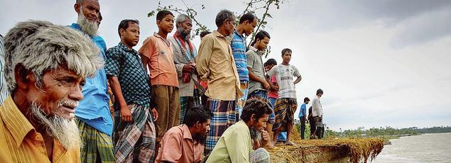 Des villageois observent avec anxiété l'érosion des côtes bordant la rivière Jamuna, en 2014 au Bangladesh.