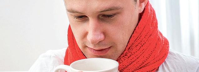 Un homme soigne son rhume avec une boisson chaude