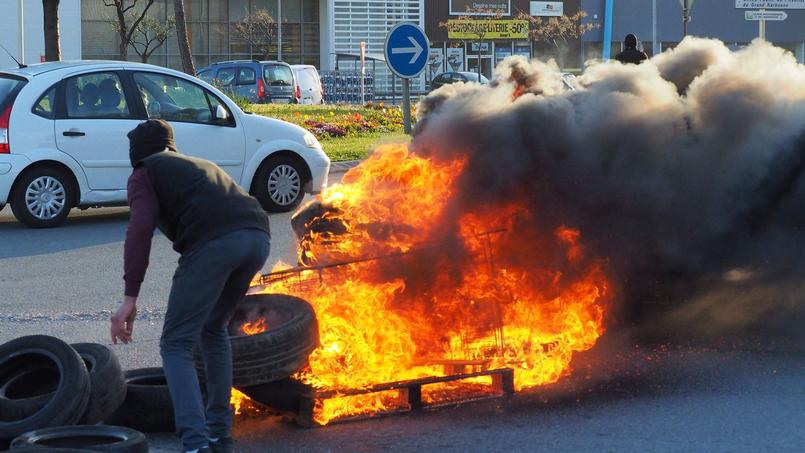 Un manifestant tente de bloquer l'accès d'une route avec un pneu brûlé.