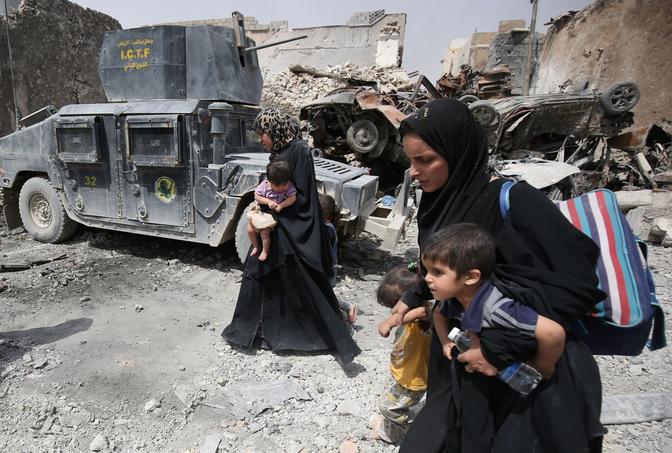 Des femmes en abaya noire fuient au milieu des ruines de la vieille ville de Mossoul avec leurs enfants dans les bras.