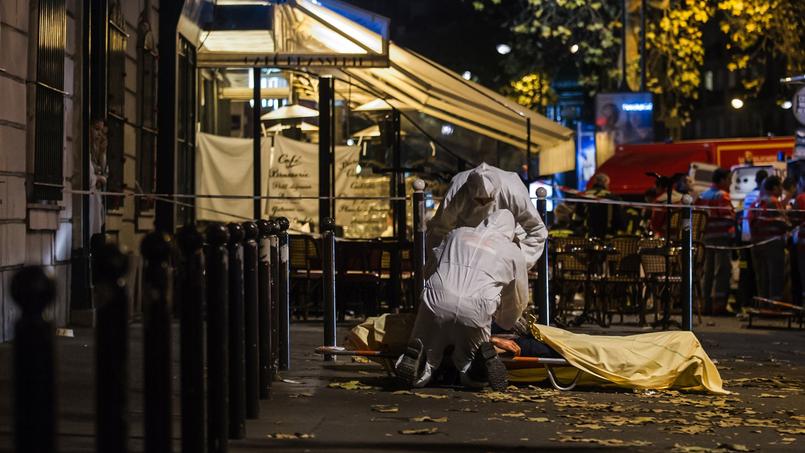 Des policiers recouvrent le corps d'une des victimes des attentats à Paris vendredi soir.