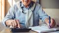 Cropped image of handsome old man using a calculator and writing in his notebook while working at home