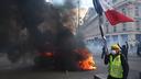 Un manifestant portant un gilet jaune et tenant un drapeau français passe devant une voiture lors d’une manifestation sur la Place de la République à Paris, le 17 octobre 2026.