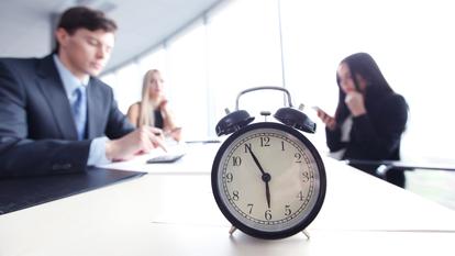 Alarm clock on office table with business discussion people group or meeting team background