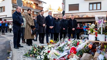 Des élus ainsi que Nicolas Feraud, maire de Crans-Montana, et Stéphane Ganzer, conseiller d’État du canton du Valais, se tiennent près des fleurs déposées en hommage aux victimes après avoir inspecté le site de l’incendie à Crans-Montana, en Suisse, le 3 janvier 2026.