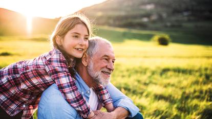 A small girl with grandfather outside in spring nature, relaxing on the grass at sunset.