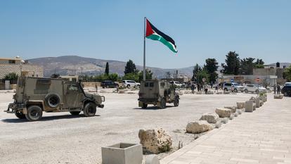 Véhicules militaires israéliens près d’un drapeau palestinien alors que des colons et des troupes visitent le site archéologique de Sébastia en Cisjordanie occupée par Israël, 29 juin 2026.