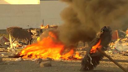 De la fumée et des flammes s’élèvent alors que des habitants de Ceuta détruisent un camp de migrants situé près de la plage.