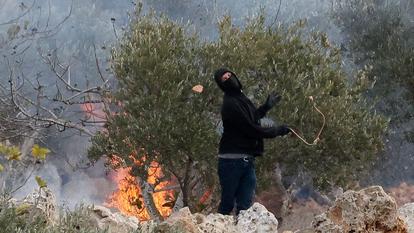 Un colon israélien lance une pierre en direction de Palestiniens, près d’un feu, lors d’affrontements survenus pendant la récolte des olives par les Palestiniens à Abu Falah, près de Ramallah, en Cisjordanie occupée par Israël, le 16 octobre 2026.