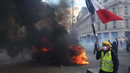 Un manifestant portant un gilet jaune et tenant un drapeau français passe devant une voiture lors d’une manifestation sur la Place de la République à Paris, le 17 octobre 2026.