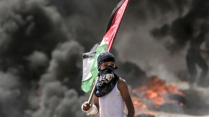 Un garçon palestinien tenant son drapeau national observe les affrontements avec les forces de sécurité israéliennes dans la bande de Gaza, le 14 mai 2018.