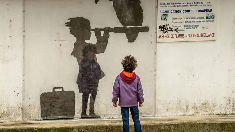 Un enfant devant un dessin de Banksy dans le camp de Calais.